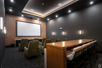 A conference room with a long table, chairs, and a screen.